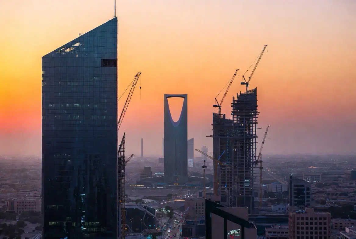 Riyadh's downtown skyline at golden hour featuring the Kingdom Centre Tower, modern glass skyscrapers under construction, and active cranes — visual evidence of the Vision 2030 mega-project boom driving demand for skilled foreign workers.